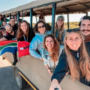 Un gruppo WeRoad sorridente posa per un selfie all'interno di un veicolo safari aperto, mostrando una bandiera sudafricana.
