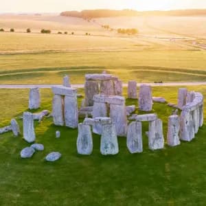 Una vista aerea del monumento di Stonehenge su un prato verde, illuminato dalla luce dorata del tramonto su campi ondulati.