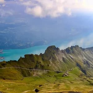 Vue aérienne d'une route sinueuse sur une crête de montagne verte, surplombant un grand lac turquoise dans une vallée.