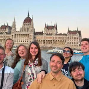 Un voyage de groupe WeRoad souriant ensemble pour une photo devant un grand bâtiment gouvernemental orné sur une rivière au crépuscule.