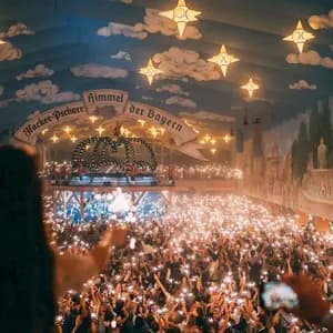 A large crowd holds up glowing sparklers inside a festive hall with a painted ceiling and star-shaped lights.