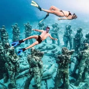 Deux membres d'un groupe WeRoad faisant de la plongée avec tuba au-dessus d'une installation circulaire de statues immergées au fond de la mer.