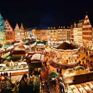 An elevated view of a bustling Christmas market at night, with a large illuminated tree, a glowing carousel, and market stalls.
