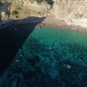 Une vue aérienne d'une crique isolée où de petits bateaux sont amarrés sur la plage et flottent dans la mer turquoise cristalline à côté de falaises abruptes.