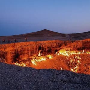Un viaggio di gruppo WeRoad si trova sul bordo di un grande cratere infuocato al tramonto, con fiamme che illuminano le pareti rocciose.