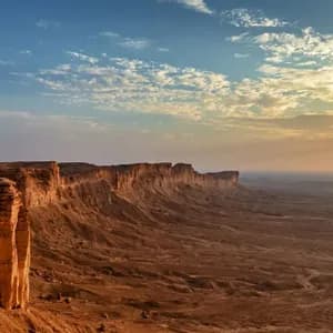 Un viaggio di gruppo WeRoad cammina lungo il bordo di una vasta scarpata rocciosa al tramonto, con vista su uno sconfinato paesaggio desertico.