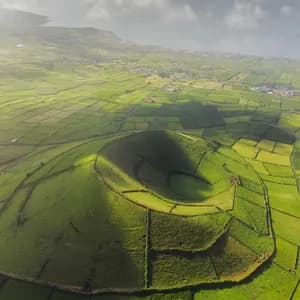 Una vista aerea di un cratere vulcanico ricoperto d'erba, circondato da un mosaico di campi verdi che si estendono verso il mare.
