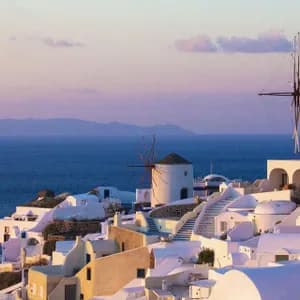 Case bianche e mulini tradizionali su una collina a picco sul mare, al tramonto colorato.