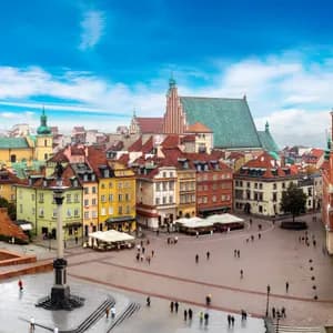 Vue plongeante sur une place de ville historique avec des bâtiments colorés, une colonne imposante et une tour horloge sous un ciel bleu éclatant.