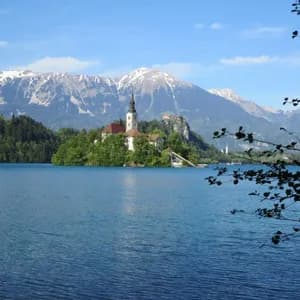 Veduta di un'isoletta con chiesa su un lago, circondata da montagne innevate sotto un cielo azzurro.
