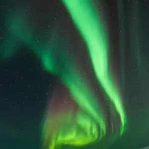 Helle grüne Bänder des Nordlichts leuchten am sternenklaren Nachthimmel über einer verschneiten Bergkette.