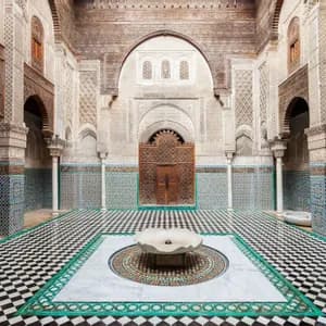 Un patio ornamentado con una fuente central sobre un suelo de baldosas a cuadros blancas y negras, rodeado de paredes con intrincados azulejos y arcos tallados.