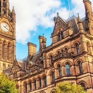 Una vista dal basso di un elaborato edificio in pietra in stile gotico con una grande torre dell'orologio, contro un cielo azzurro con nuvole.