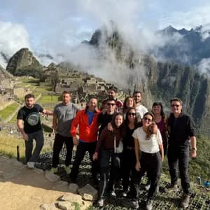 Un grupo de WeRoad posa para una foto con ruinas de piedra antiguas y montañas cubiertas de nubes al fondo.