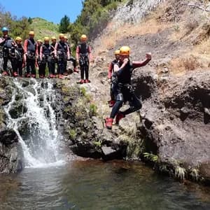 Una persona di un viaggio di gruppo WeRoad, con muta e casco, si tuffa in una piscina naturale vicino a una cascata mentre altri guardano.