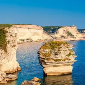 Eine große, geschichtete Felsformation liegt im blauen Meer neben weißen Küstenklippen unter einem klaren Himmel.