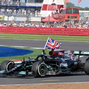 A black Formula 1 race car with a British flag attached drives around a track in front of spectators in the stands.