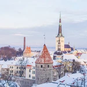 Uno skyline di una città storica in inverno, con tetti coperti di neve, torri di pietra con tetti rossi e un'alta guglia di chiesa.