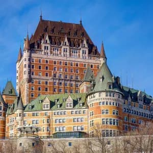 Un grand hôtel aux allures de château, avec des murs de briques, des toits pentus verts et bruns, et de nombreuses tourelles, se dresse sous un ciel bleu clair.