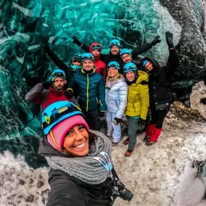 A smiling WeRoad group trip wearing helmets takes a selfie inside a vibrant turquoise ice cave.