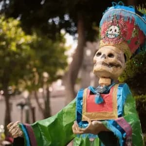 Un squelette décoratif vêtu d'un costume coloré et d'une coiffe haute et élaborée ornée d'un emblème de crâne, se dresse dans un parc.