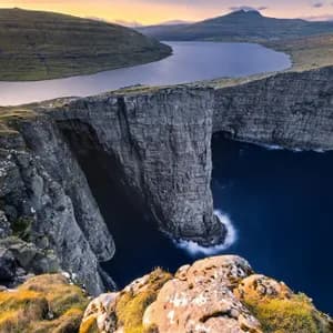 Un grande lago si trova sul bordo di un'alta scogliera, affacciato sul profondo oceano blu, con verdi colline ondulate in lontananza.