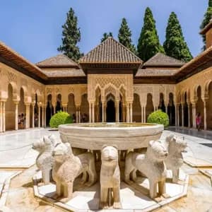 Una fuente de piedra con estatuas de leones se alza en un soleado patio de estilo morisco rodeado de columnatas arqueadas.
