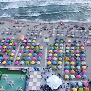 Vista aerea di una spiaggia affollata con file di ombrelloni colorati disposti sulla sabbia accanto al mare.