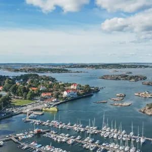 Eine Luftaufnahme einer Marina voller Boote an einer Küste mit felsigen Inseln unter blauem, bewölktem Himmel.