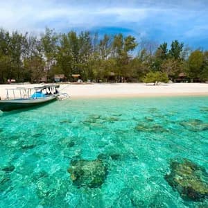 Ein Boot ankert in flachem, klarem türkisfarbenem Wasser vor einem weißen Sandstrand, der von üppigen grünen Bäumen gesäumt wird, unter einem blauen Himmel.