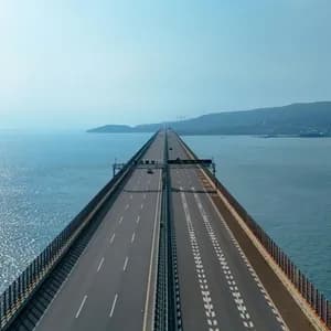 A long highway bridge extends over the sea towards a distant, hazy shoreline.