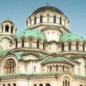 A large cathedral with a central golden dome and multiple green domes against a clear blue sky.