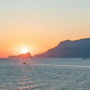 Una barca naviga sul mare durante un tramonto vivace, con isole rocciose stagliate contro il cielo arancione.