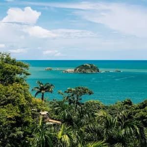 Una vista su una lussureggiante volta della giungla di una piccola isola rocciosa in un oceano turchese sotto un cielo blu con nuvole.