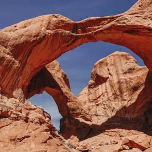 Two large, overlapping red rock arches form a double arch against a cloudless blue sky.