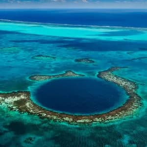 Una vista aerea di una vasta dolina marina blu scuro, circondata da un atollo corallino in un oceano turchese poco profondo.