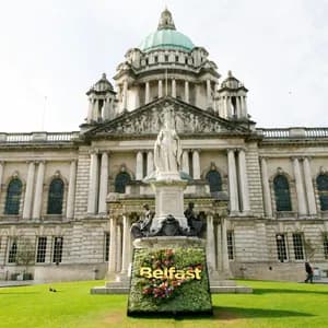 Un'insegna floreale 'Belfast' e una statua sul prato davanti al grandioso Municipio di Belfast.