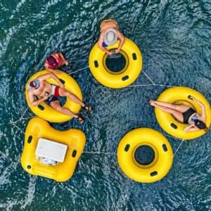 A WeRoad group trip of people relaxing on yellow inflatable rings tied together in dark blue water, seen from above.