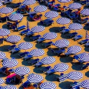 Una vista dall'alto di ombrelloni e lettini a strisce blu e bianche che creano un motivo su una spiaggia di sabbia.