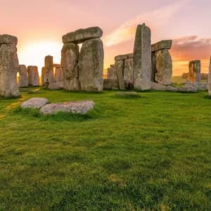 The large standing stones of the Stonehenge monument on a grassy field under a glowing sunrise sky.