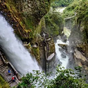 Una potente cascata che scorre lungo una gola rocciosa accanto a una scalinata in pietra serpeggiante con persone che vi camminano sopra.