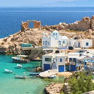 Un villaggio costiero con case imbiancate e una chiesa, incastonato in una cala rocciosa con barche in una baia turchese.