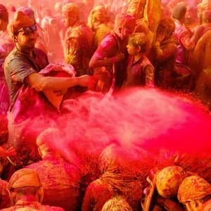 Un uomo con il turbante lancia una nuvola di polvere rossa su una fitta folla di persone, anch'esse ricoperte di polvere colorata.
