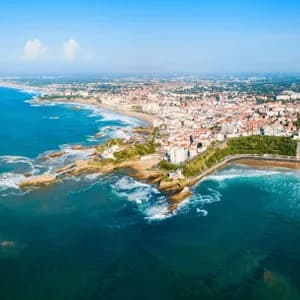 Veduta aerea di una città costiera, con una lunga spiaggia sabbiosa e una costa rocciosa che si affaccia sull'oceano blu.