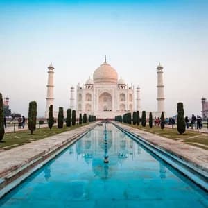 A long reflecting pool leads to a large white marble mausoleum with minarets, surrounded by gardens where people are walking.