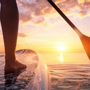 Vista dal basso di una persona che fa stand-up paddle sul mare calmo durante un tramonto vibrante.