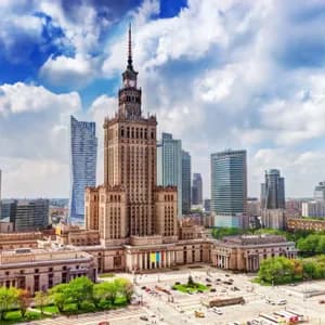 Vista aerea di un grattacielo storico circondato da edifici moderni in un centro città sotto un cielo parzialmente nuvoloso.