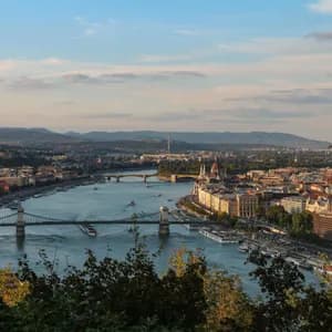 Una veduta aerea di una città attraversata da un grande fiume, solcato da diversi ponti, con colline sullo sfondo sotto un cielo blu.