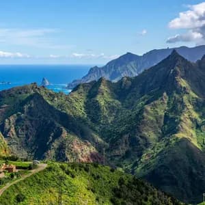 Una vista panoramica e ampia di aspre montagne verdi lungo una costa, che si uniscono a un mare blu intenso sotto un cielo parzialmente nuvoloso.