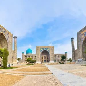 A panoramic view of a large, historic square flanked by three ornate buildings with intricate tilework, tall minarets, and blue domes.